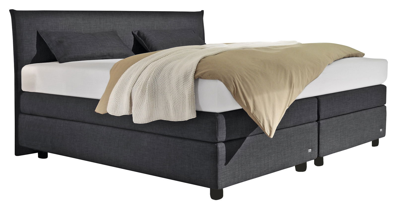 Boxspringbett in dunklem Stoffbezug mit zwei Kissen und einer Decke, seitliche Perspektive