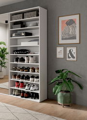 Weißes Schuhregal mit mehreren Fächern, gefüllt mit verschiedenen Schuhen und Accessoires, in einem modernen Raum mit Pflanzen und Wanddekorationen. Perspektive von vorne links.