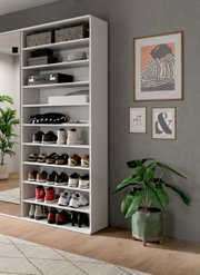 Weißes Schuhregal mit mehreren Fächern, gefüllt mit verschiedenen Schuhen und Accessoires, in einem modernen Raum mit Pflanzen und Wanddekorationen. Perspektive von vorne links.
