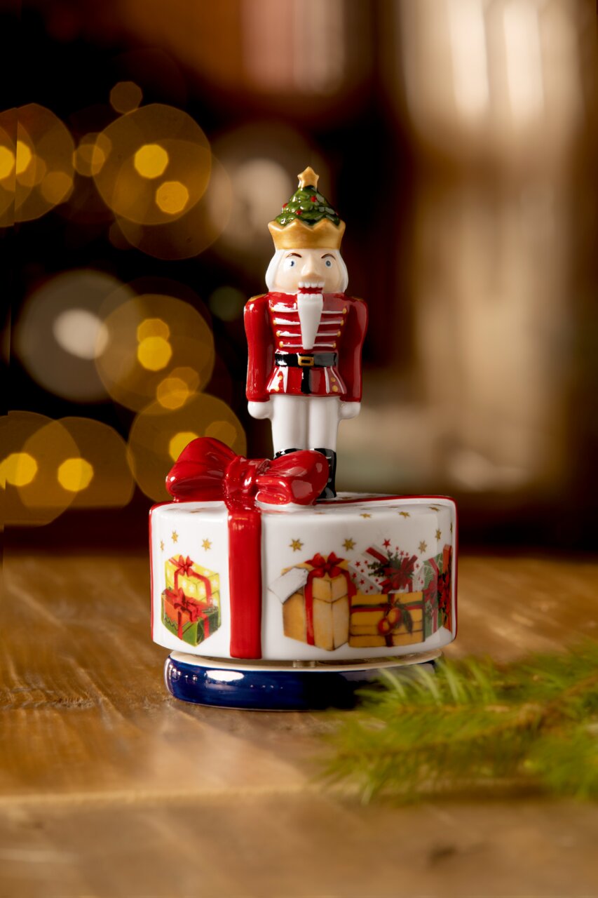Spieluhr in Form eines Nussknackers, der auf einem dekorativen Sockel mit Geschenk- und Schleifenmotiven steht, aus der Perspektive von vorne fotografiert.