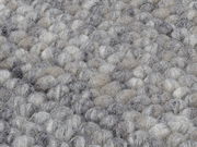 Nahaufnahme eines handgewebten Teppichs mit einer texturierten, grauen und beigen Oberfläche.