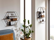 Frontalansicht eines modernen, schwarzen Wandregals aus Metall in ovaler Form mit mehreren Ablagen, dekoriert mit Skulptur, Vase und Korb, montiert an einer hellen Wand neben einem Fenster.