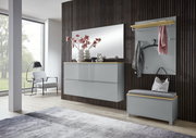 Modernes Garderoben-Set im Flur mit grauer Hochglanz-Kommode, großem Wandspiegel, Garderobenpaneel mit Haken und Ablage sowie Sitzbank mit Polster, frontal in leichter Schrägansicht von links fotografiert.