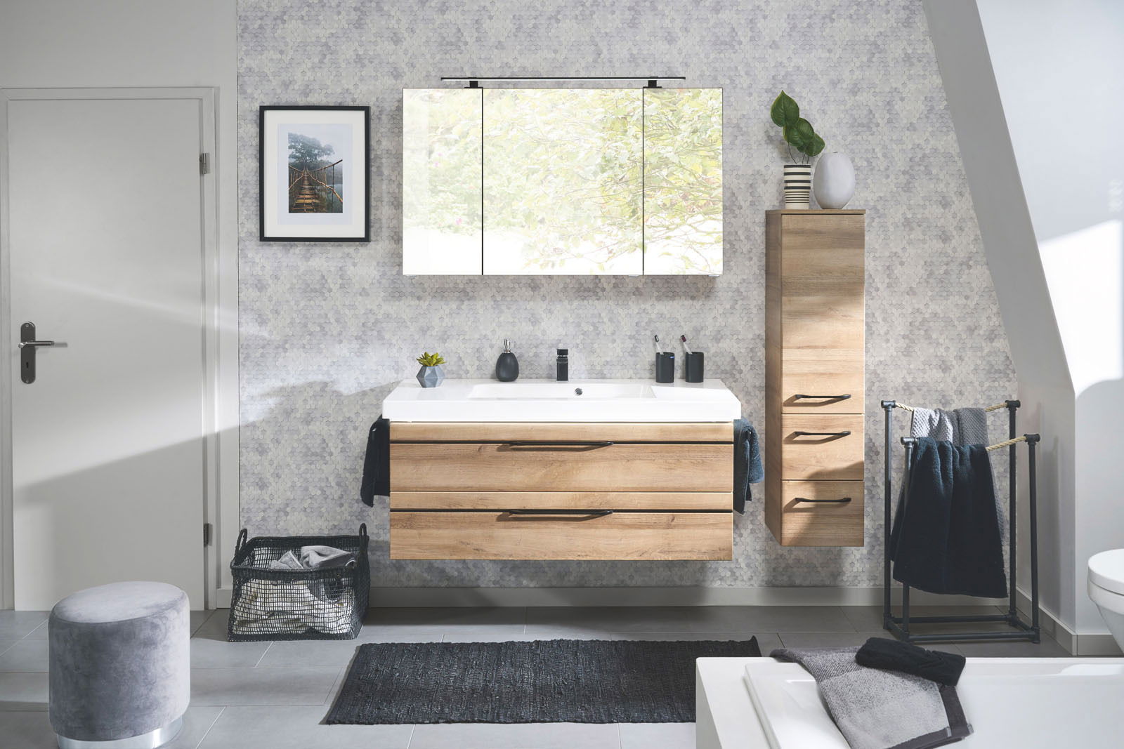 Moderne Badkombination mit Holzoptik, bestehend aus einem Waschtisch mit zwei Schubladen, einem großen Spiegel und einem hohen Schrank, frontal aufgenommen.