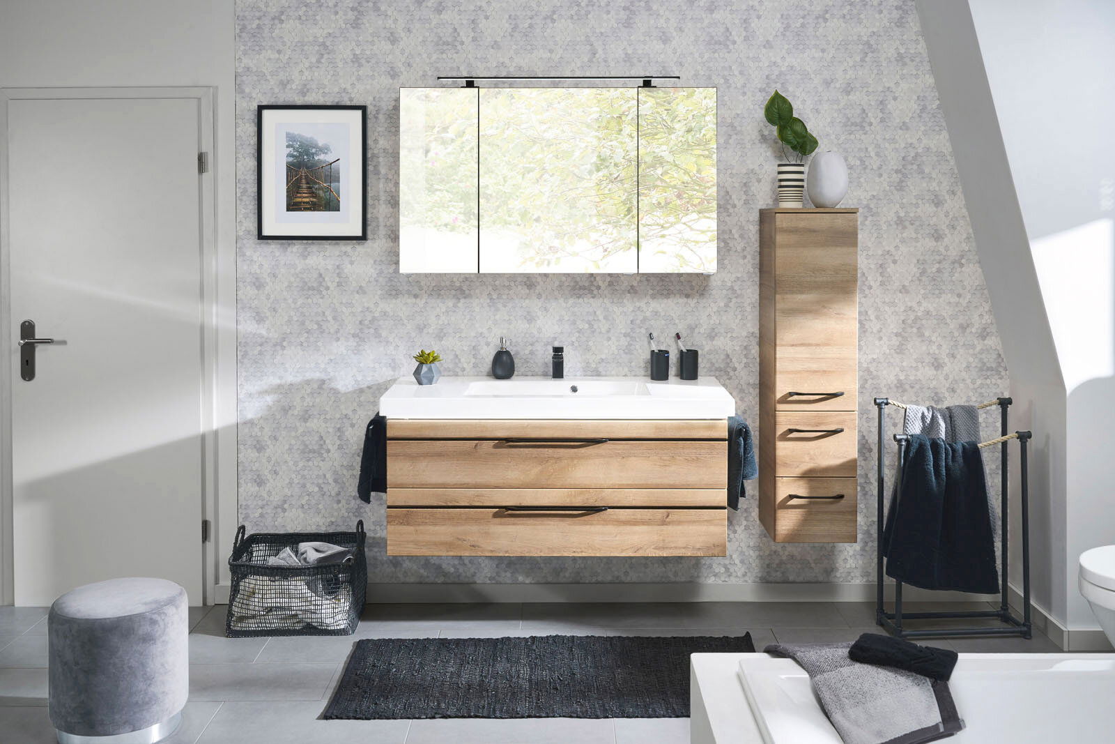 Moderne Badkombination mit Holzoptik, bestehend aus einem Waschtisch mit zwei Schubladen, einem großen Spiegel und einem hohen Schrank, frontal aufgenommen.