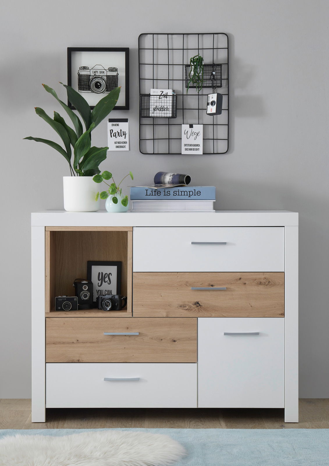 Moderne Kommode in Weiß und Holzoptik mit mehreren Schubladen, dekoriert mit Pflanzen und Büchern, frontal fotografiert.