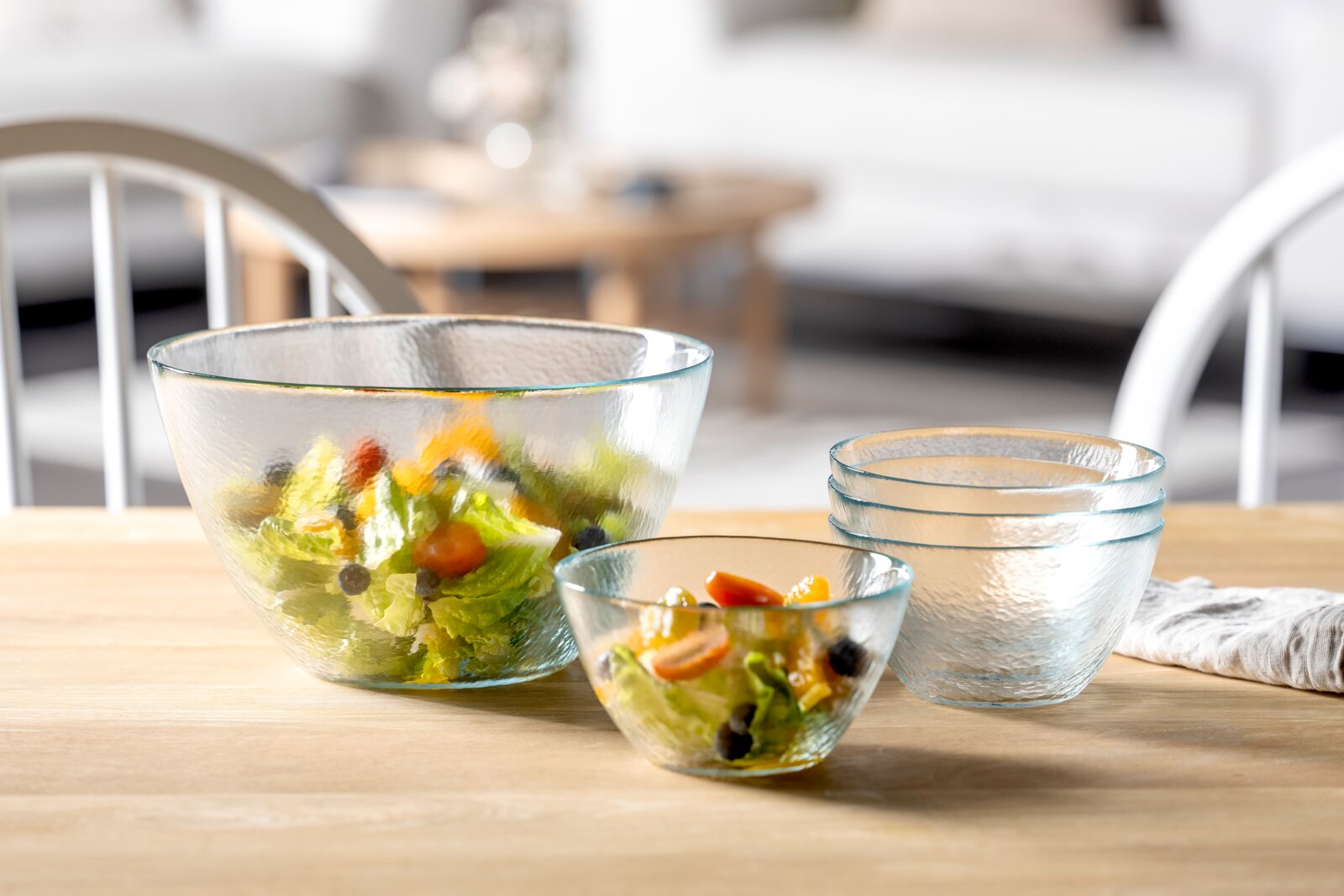 Ein 5-teiliges Schalenset aus Glas, bestehend aus verschiedenen Größen, präsentiert auf einem Tisch. Die Schalen sind teilweise mit frischem Salat gefüllt. Perspektive: seitlich von vorne.