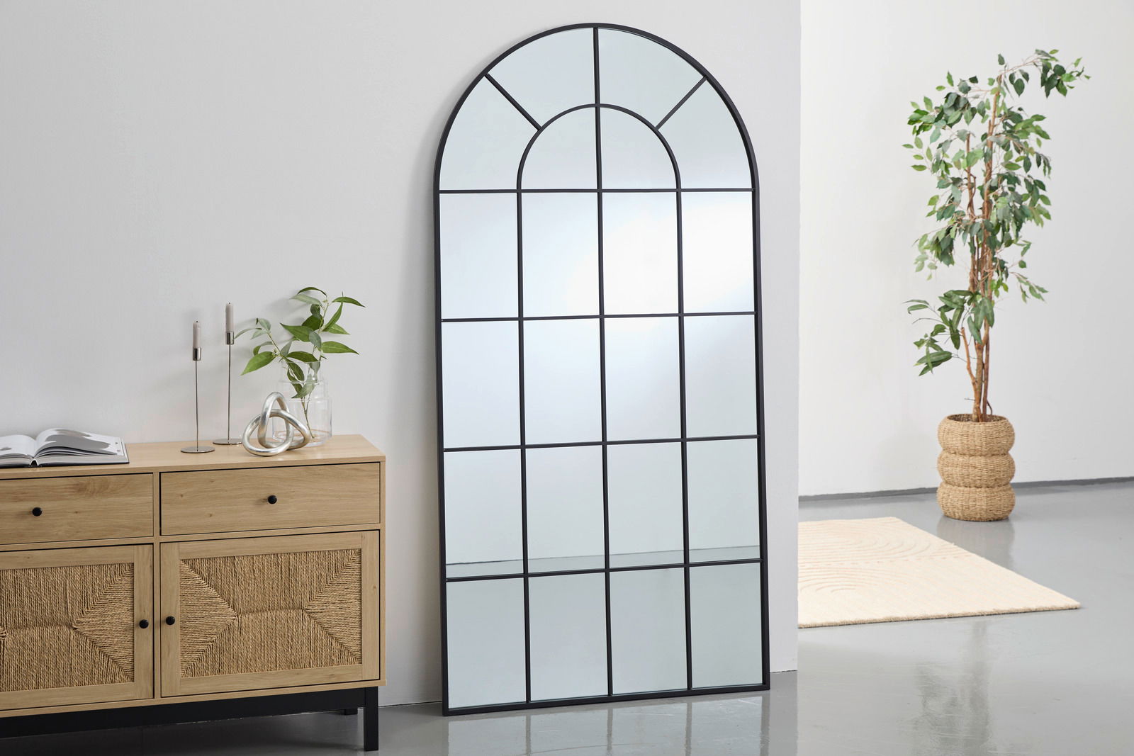 Landscape Spiegel CARLO Großer, rechteckiger Spiegel mit schwarzem Rahmen und Gittermuster, an eine weiße Wand gelehnt, neben einer Holzkommode und einer Pflanze. Perspektive von vorne.