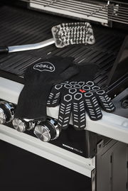 Schwarze Premium Grillhandschuhe mit rutschfestem Muster, auf einem Grill liegend, seitliche Perspektive.