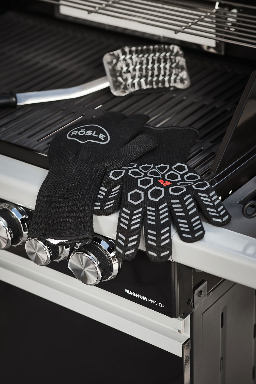 Schwarze Premium Grillhandschuhe mit rutschfestem Muster, auf einem Grill liegend, seitliche Perspektive.