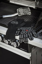 Schwarze Premium Grillhandschuhe mit rutschfestem Muster, auf einem Grill liegend, seitliche Perspektive.