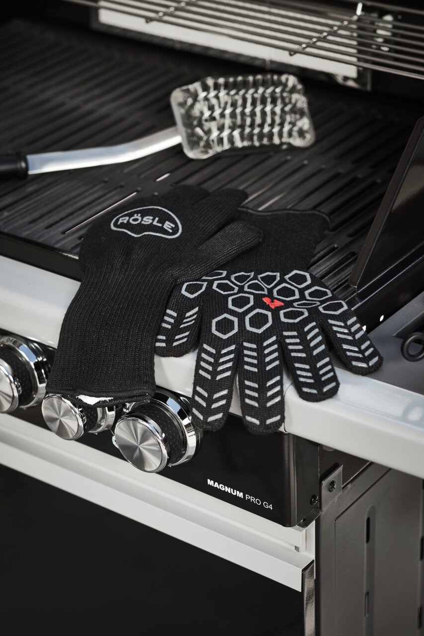 Rösle Premium Grillhandschuhe BBQ Schwarze Premium Grillhandschuhe mit rutschfestem Muster, auf einem Grill liegend, seitliche Perspektive.