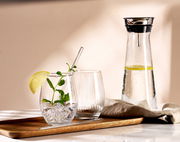 Ein stilvolles Partyset bestehend aus einem Tablett mit zwei Gläsern, eines mit Minze und Limettenscheibe, und einer Karaffe mit Wasser und Limettenscheiben, aus seitlicher Perspektive fotografiert.