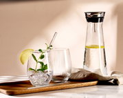 Ein stilvolles Partyset bestehend aus einem Tablett mit zwei Gläsern, eines mit Minze und Limettenscheibe, und einer Karaffe mit Wasser und Limettenscheiben, aus seitlicher Perspektive fotografiert.