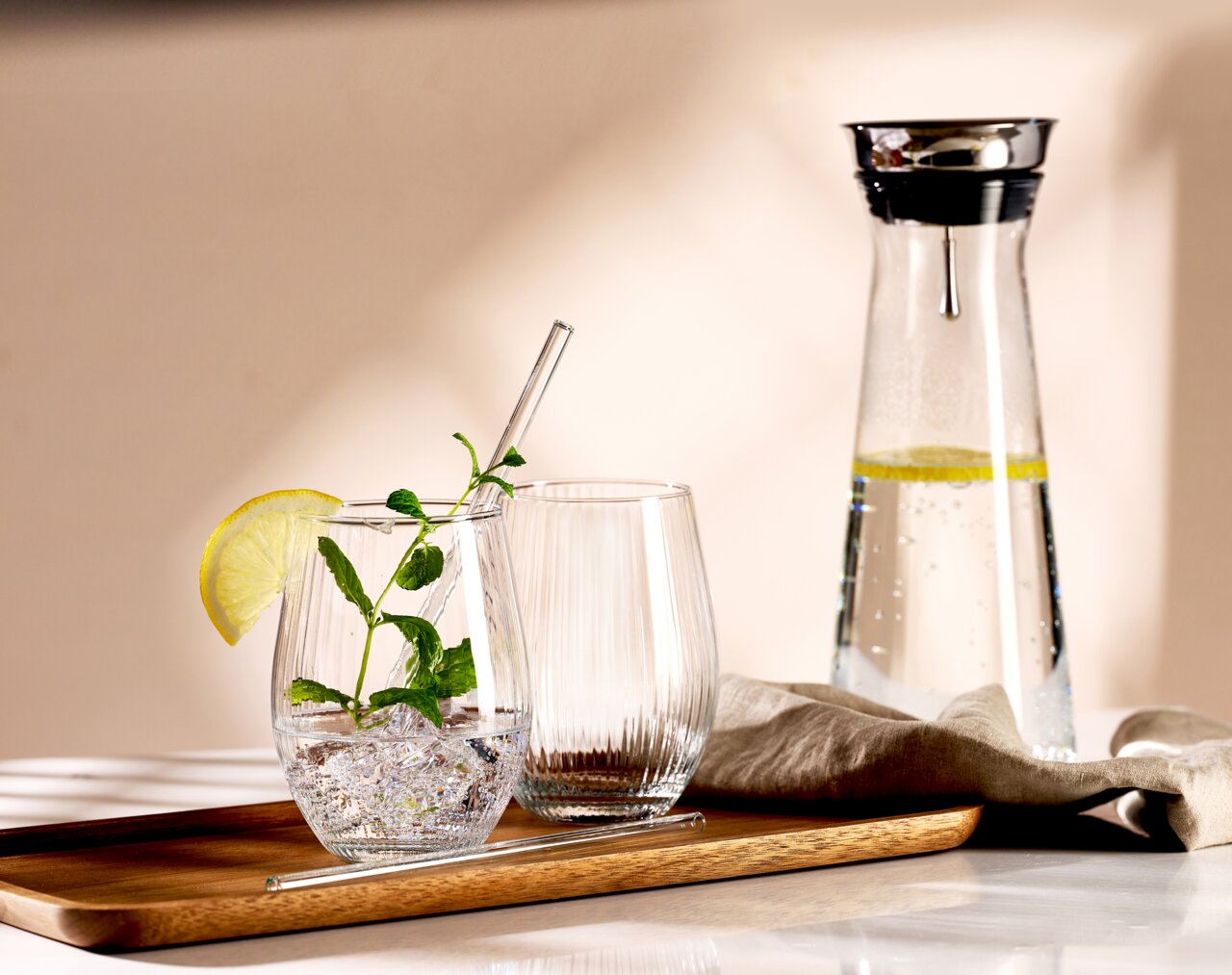 Ein stilvolles Partyset bestehend aus einem Tablett mit zwei Gläsern, eines mit Minze und Limettenscheibe, und einer Karaffe mit Wasser und Limettenscheiben, aus seitlicher Perspektive fotografiert.