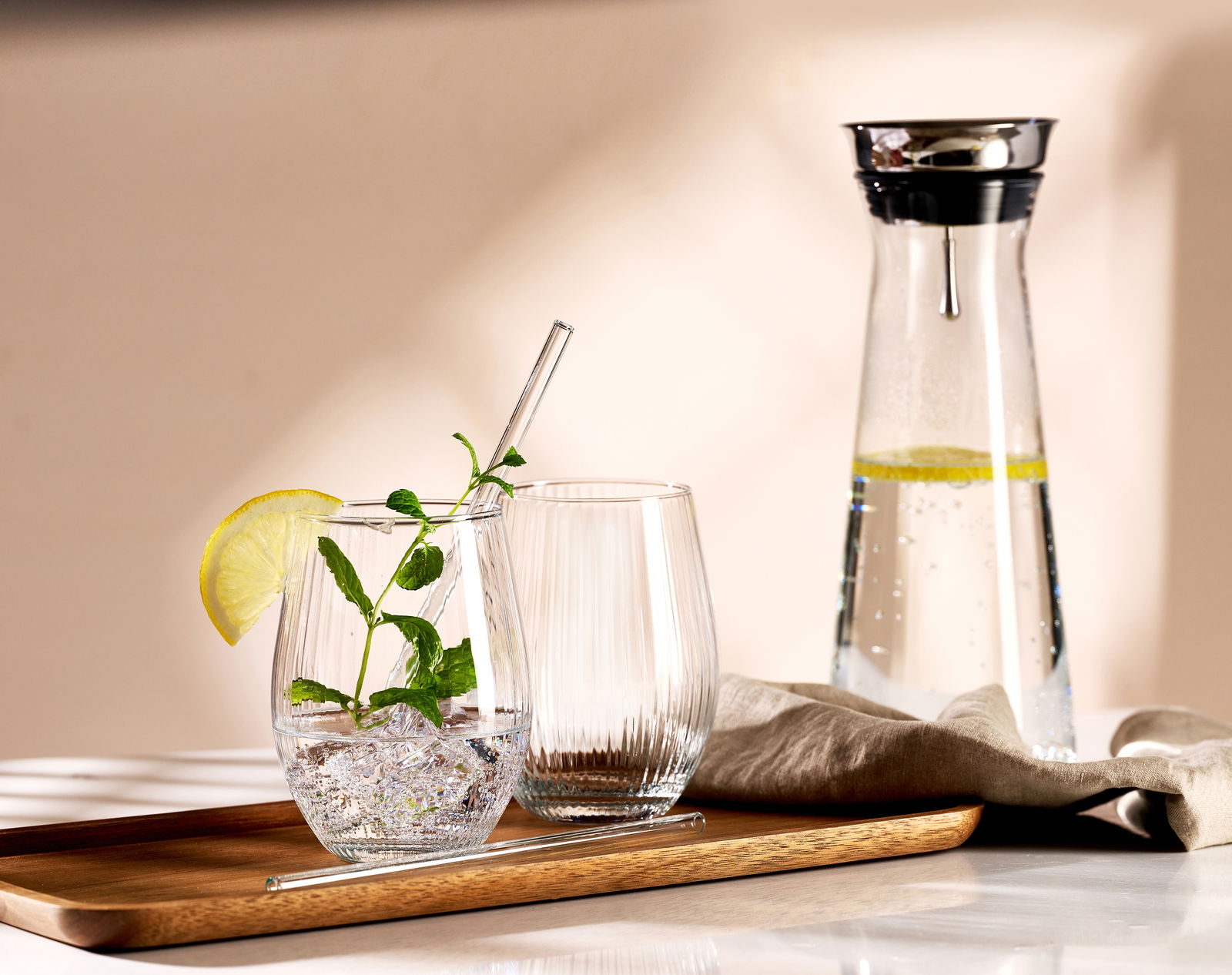 Ein stilvolles Partyset bestehend aus einem Tablett mit zwei Gläsern, eines mit Minze und Limettenscheibe, und einer Karaffe mit Wasser und Limettenscheiben, aus seitlicher Perspektive fotografiert.