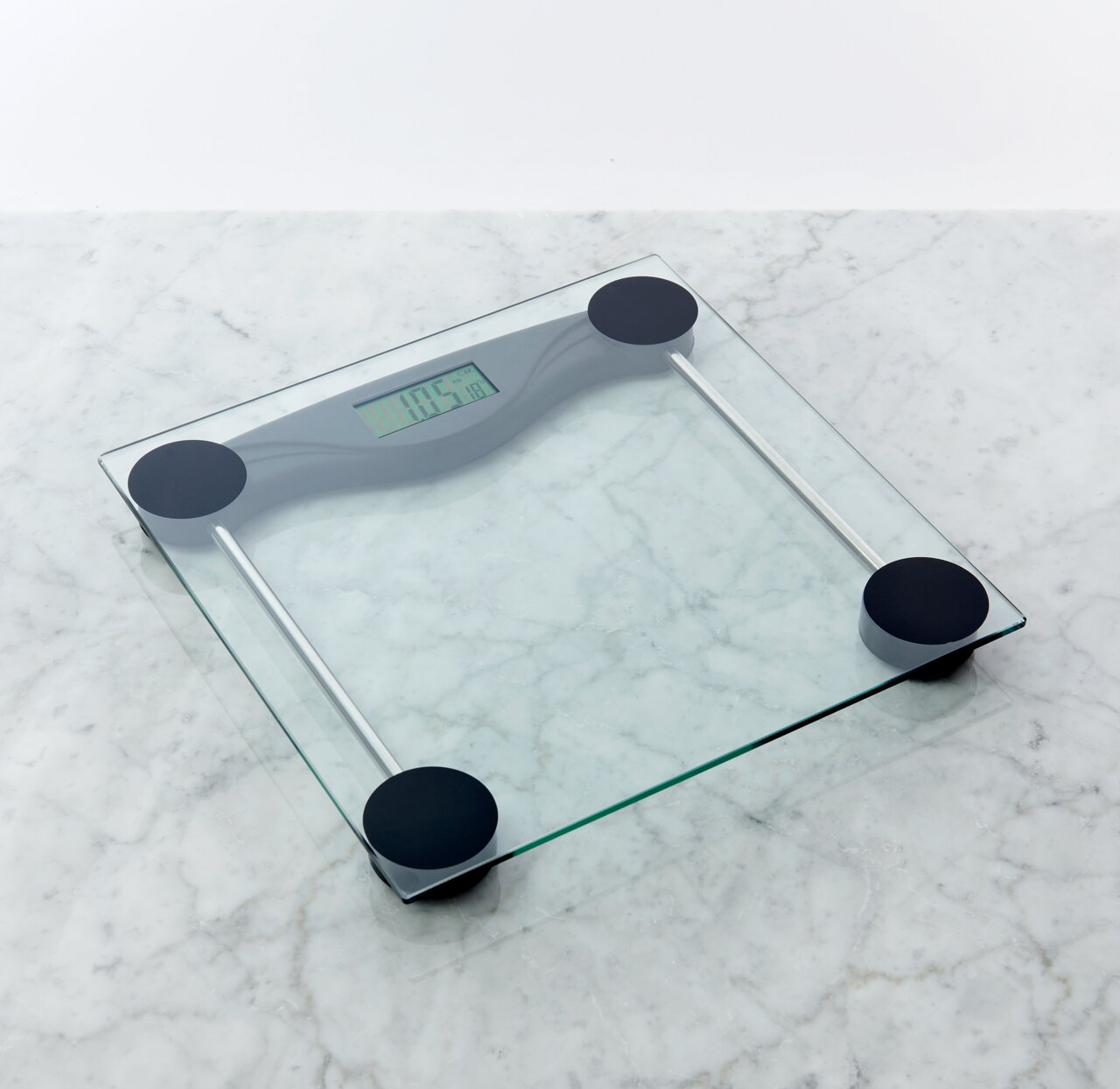 Digitale personenweegschaal van transparant glas met vier zwarte poten en een LCD-display, schuin van bovenaf gefotografeerd op een licht marmeren oppervlak.