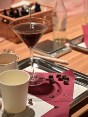 Donkere kaars in een cocktailglas met kleine chocolade-elementen tijdens een creatieve DIY-workshop.