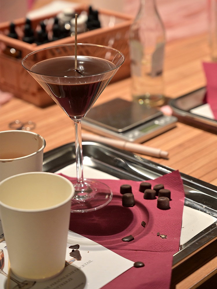 Donkere kaars in een cocktailglas met kleine chocolade-elementen tijdens een creatieve DIY-workshop.