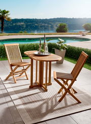 Zwei Holzklappstühle und ein passender Tisch auf einer Terrasse mit Blick auf einen Pool und eine malerische Landschaft im Hintergrund, aus seitlicher Perspektive.