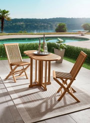 Twee houten klapstoelen en een bijpassende tafel op een terras met uitzicht op een zwembad en een schilderachtig landschap op de achtergrond, gezien vanuit een zijdelingse hoek.