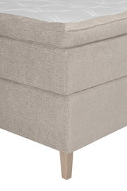Nahaufnahme eines Boxspringbettes in Beige mit Holzfuß, seitliche Perspektive