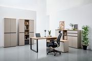 Moderne Büromöbel in einem hellen Raum, bestehend aus einem Winkelschreibtisch mit Laptop, einem ergonomischen Bürostuhl und mehreren Aktenschränken. Perspektive von vorne.