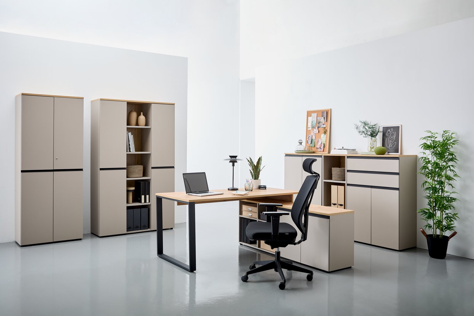 Moderne Büromöbel in einem hellen Raum, bestehend aus einem Winkelschreibtisch mit Laptop, einem ergonomischen Bürostuhl und mehreren Aktenschränken. Perspektive von vorne.