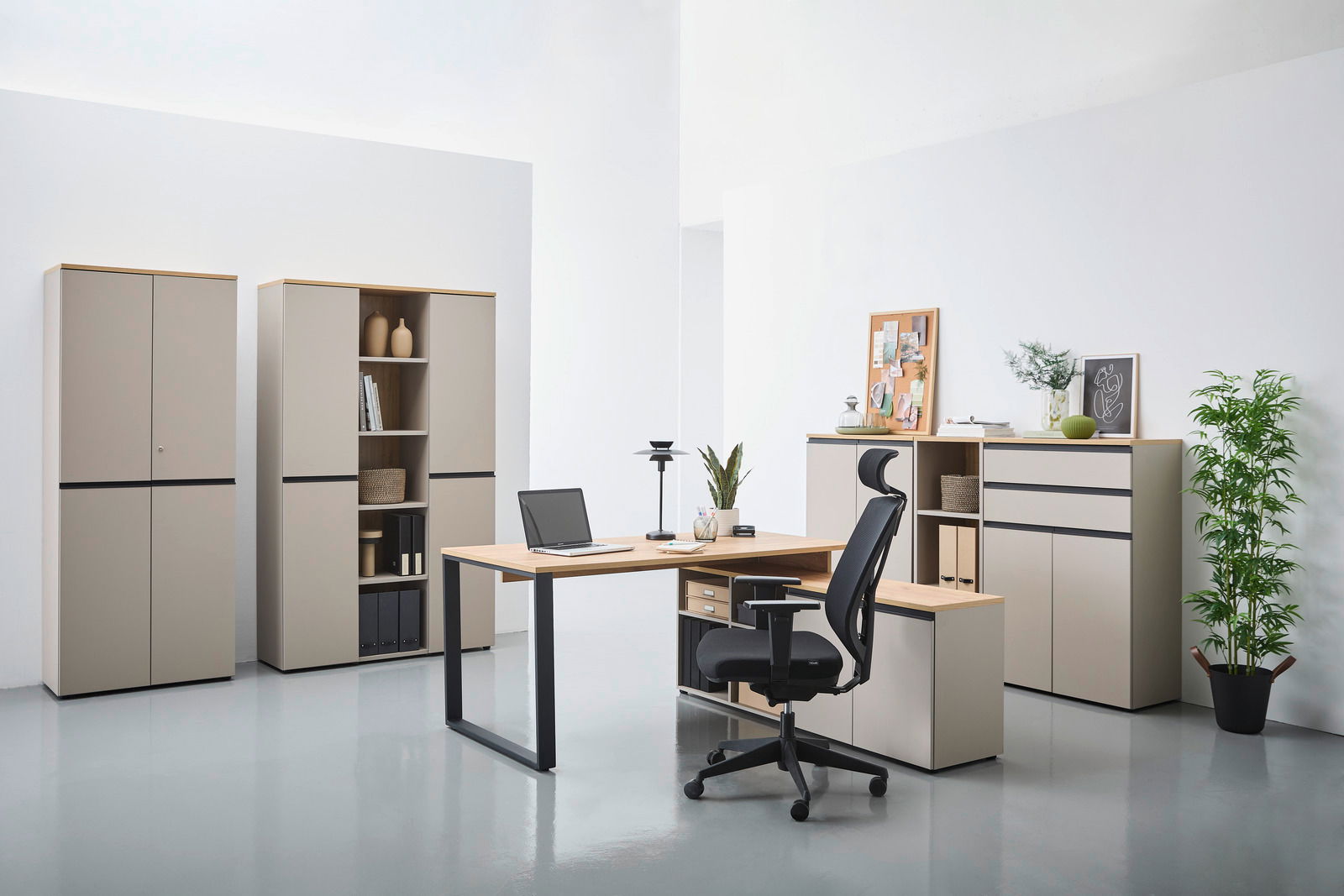 Moderne Büromöbel in einem hellen Raum, bestehend aus einem Winkelschreibtisch mit Laptop, einem ergonomischen Bürostuhl und mehreren Aktenschränken. Perspektive von vorne.