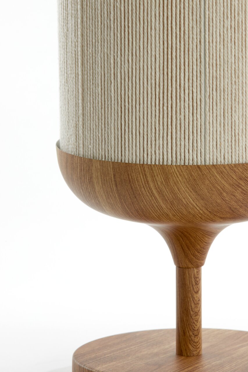Detailfoto van een tafellamp met een cilindervormige, crèmekleurige stoffen kap en een houten voet in warm bruin, zijaanzicht van dichtbij tegen een witte achtergrond