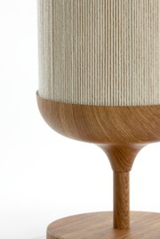 Detailfoto van een tafellamp met een cilindervormige, crèmekleurige stoffen kap en een houten voet in warm bruin, zijaanzicht van dichtbij tegen een witte achtergrond