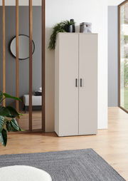 Moderner XL-Schuhschrank in heller Farbe, frontal fotografiert, mit Pflanzen und Dekoration auf der Oberseite, in einem stilvollen Raum mit Holzboden und großen Fenstern.