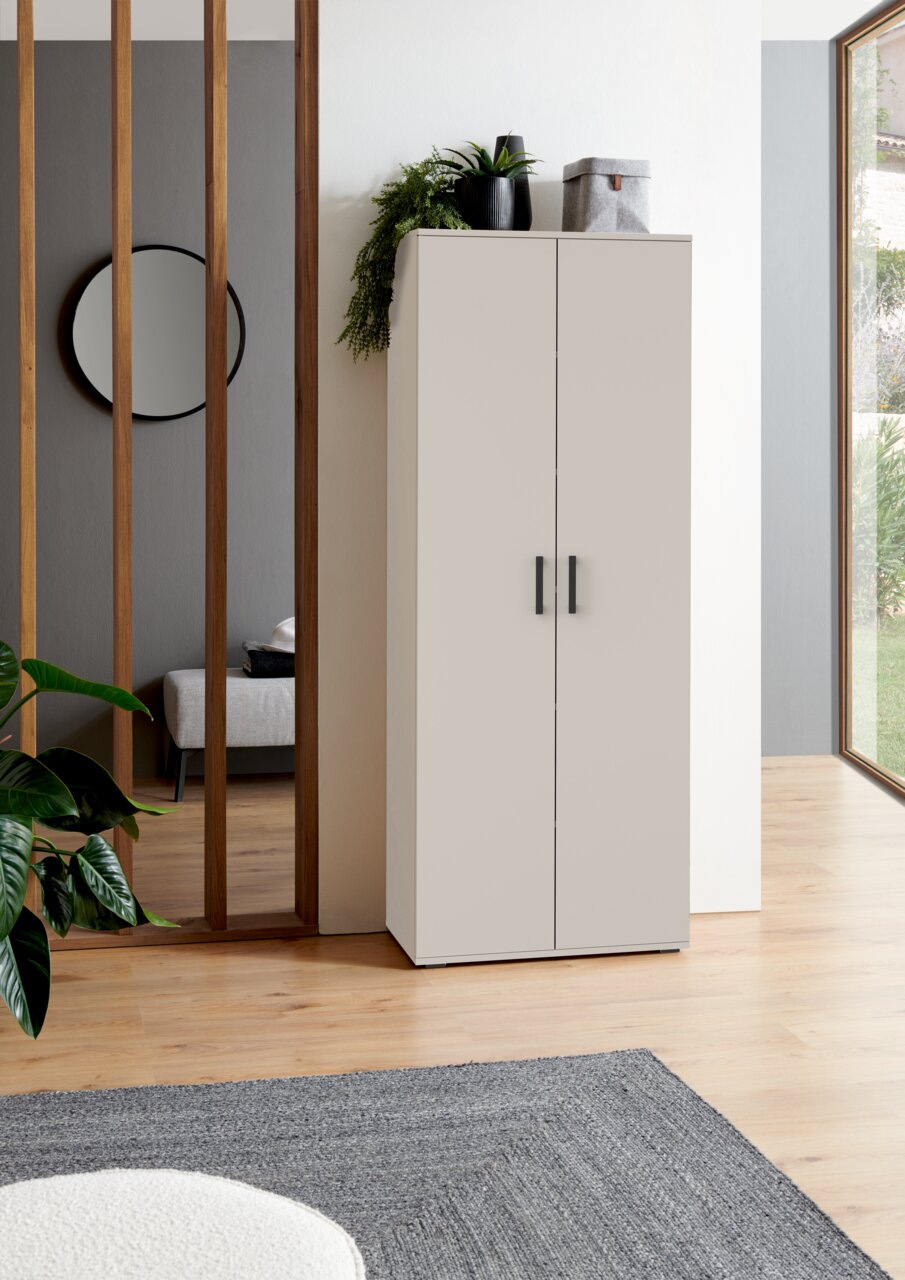 Moderner XL-Schuhschrank in heller Farbe, frontal fotografiert, mit Pflanzen und Dekoration auf der Oberseite, in einem stilvollen Raum mit Holzboden und großen Fenstern.