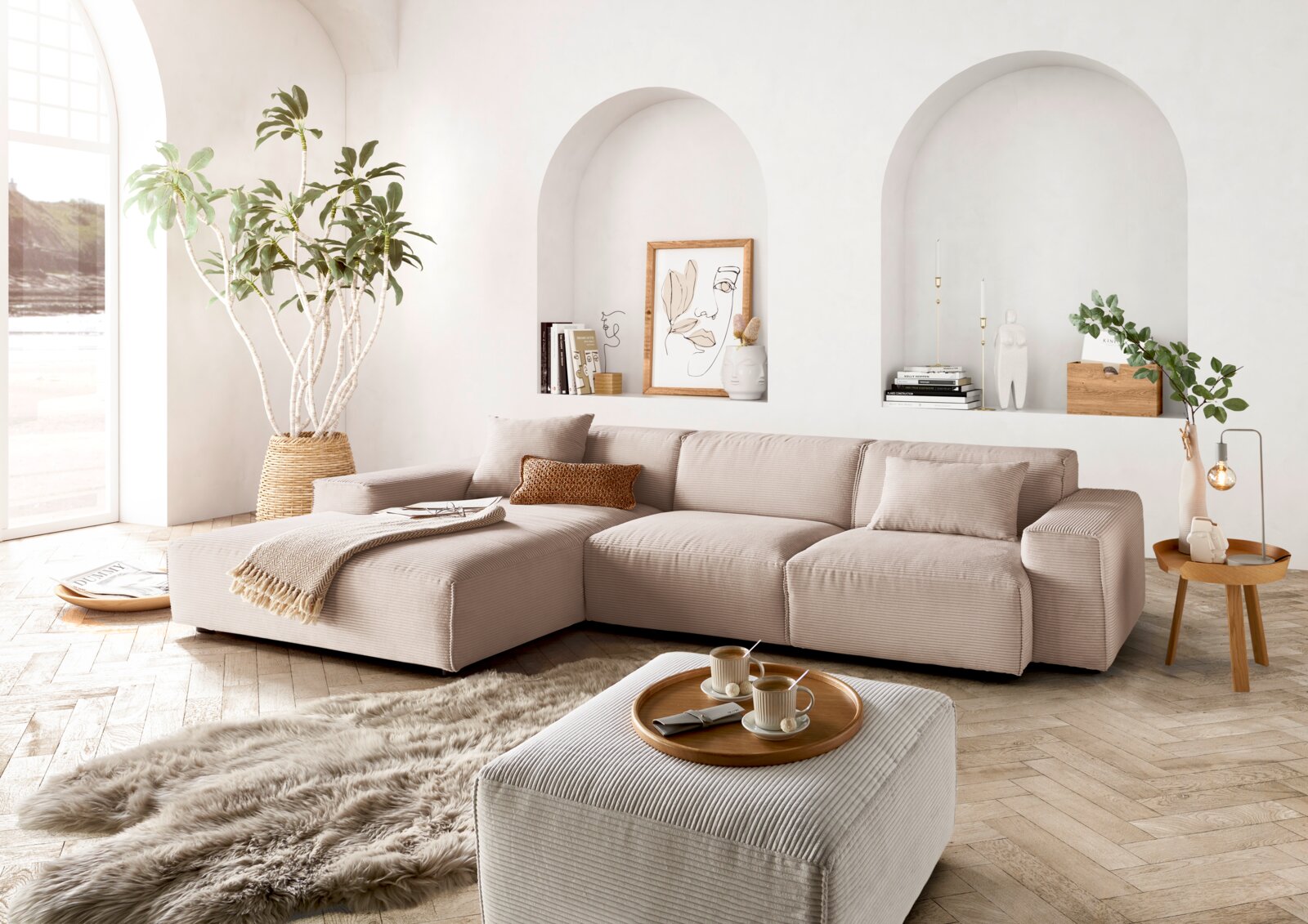 Moderne beige Ecksofa in einem hellen Wohnzimmer mit großen Fenstern, Pflanzen und stilvollen Dekorationen, aus der Perspektive von vorne links.