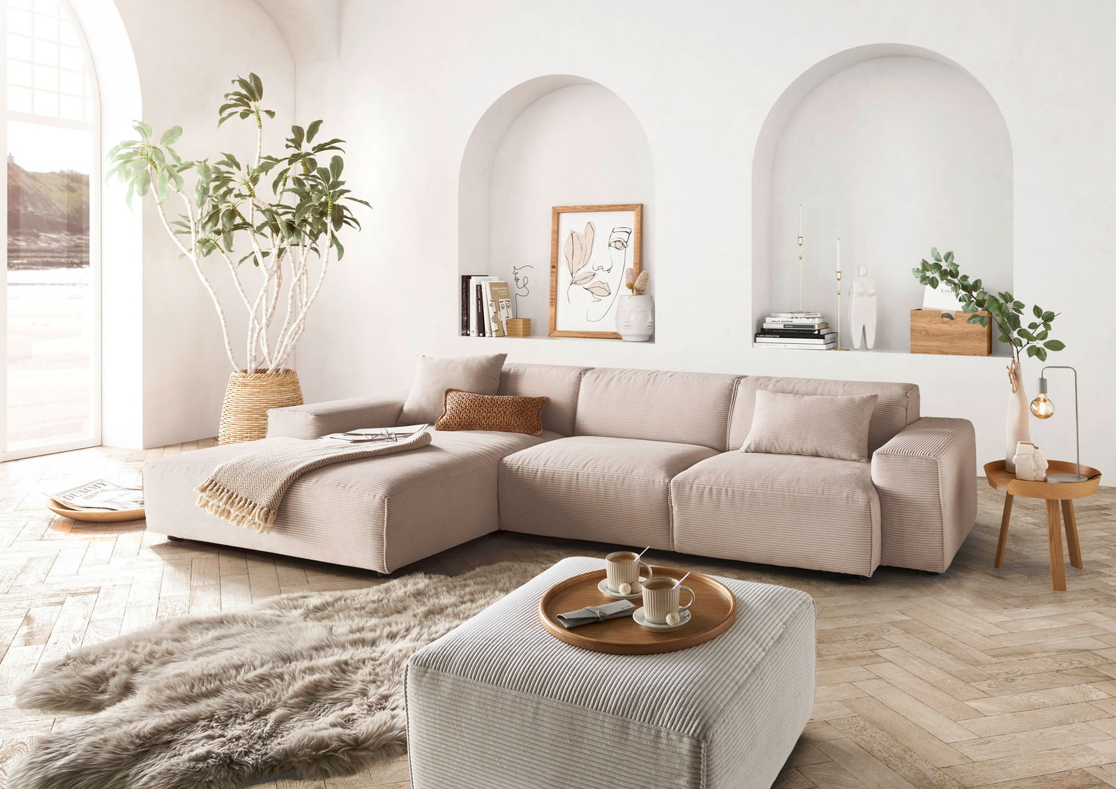 Moderne beige Ecksofa in einem hellen Wohnzimmer mit großen Fenstern, Pflanzen und stilvollen Dekorationen, aus der Perspektive von vorne links.