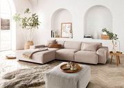 Moderne beige Ecksofa in einem hellen Wohnzimmer mit großen Fenstern, Pflanzen und stilvollen Dekorationen, aus der Perspektive von vorne links.
