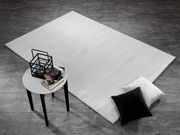 Moderner Wollteppich in hellem Grau auf dunklem Fliesenboden, mit schwarzem und weißem Kissen sowie einem kleinen Tisch mit Büchern und Dekoration. Perspektive von oben.