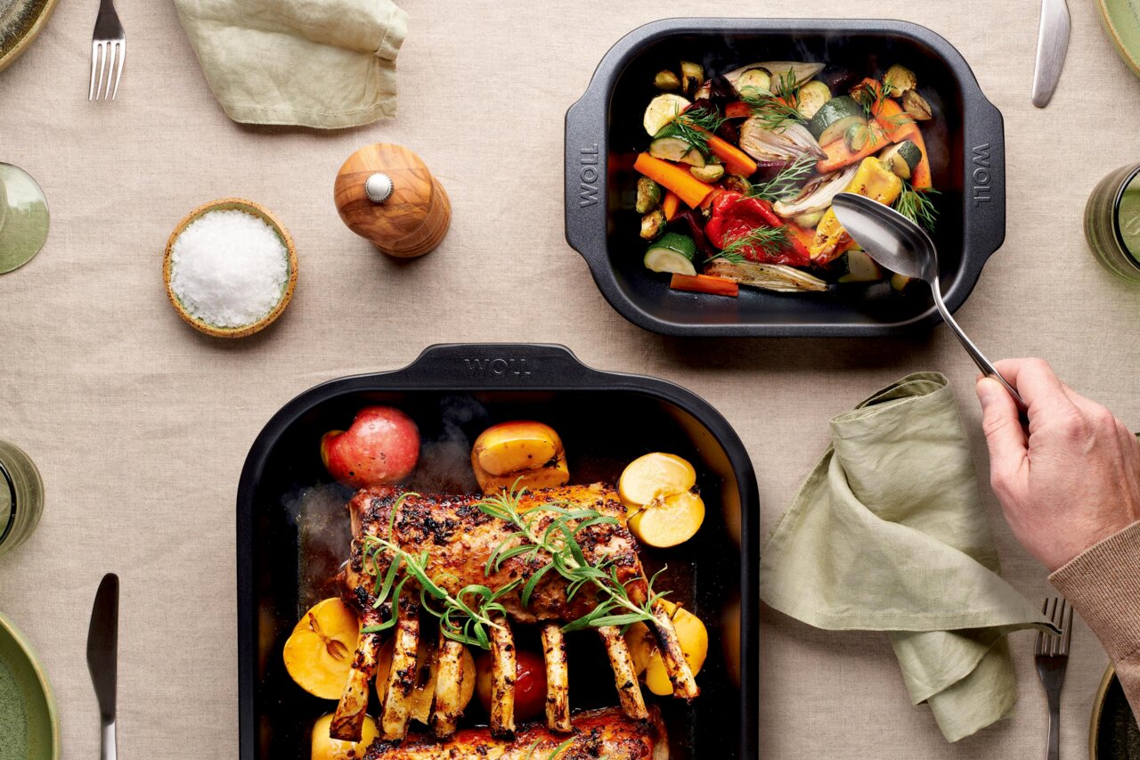 Woll Bratreine ROAST IT Zwei Bratreinen aus schwarzem Material, gefüllt mit gebratenem Gemüse und Fleisch, auf einem gedeckten Tisch von oben betrachtet.