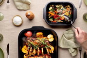 Zwei Bratreinen aus schwarzem Material, gefüllt mit gebratenem Gemüse und Fleisch, auf einem gedeckten Tisch von oben betrachtet.