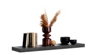 Wandboard mit Dekoration, darunter Bücher, eine Vase mit Pampasgras und schwarze Schalen, seitliche Perspektive