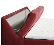 Nahaufnahme eines Boxspringbetts mit rotem Stoffbezug und geöffneter Stauraumfunktion, seitliche Perspektive