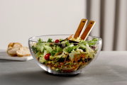 Glasklare Schale mit frischem Salat und Holzsalatbesteck, seitliche Perspektive
