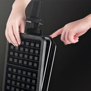 Nahaufnahme eines Waffeleisens Professional, das von zwei Händen gehalten wird. Die Perspektive zeigt das Gerät in einem leicht geöffneten Zustand von der Seite.