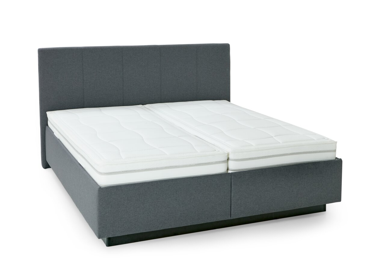 Graues Polsterbett mit hohem Kopfteil und zwei weißen Matratzen, seitliche Perspektive