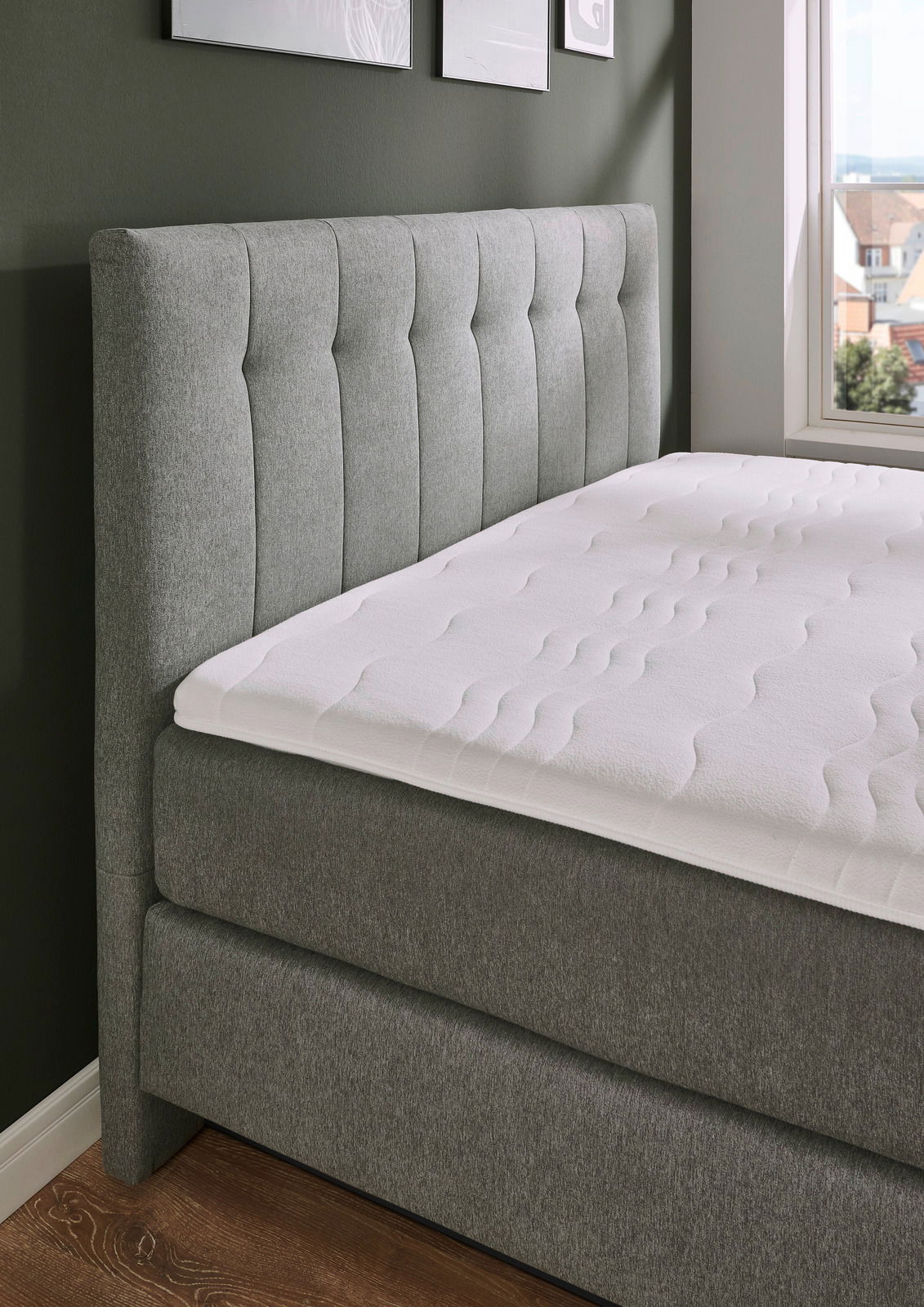 Boxspringbett BX 180/200 in grauem Stoffbezug, seitliche Perspektive mit Blick auf das gepolsterte Kopfteil und die Matratze.