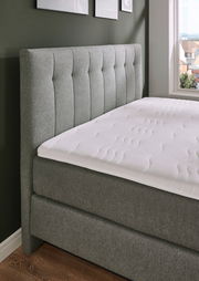 Boxspringbett BX 180/200 in grauem Stoffbezug, seitliche Perspektive mit Blick auf das gepolsterte Kopfteil und die Matratze.