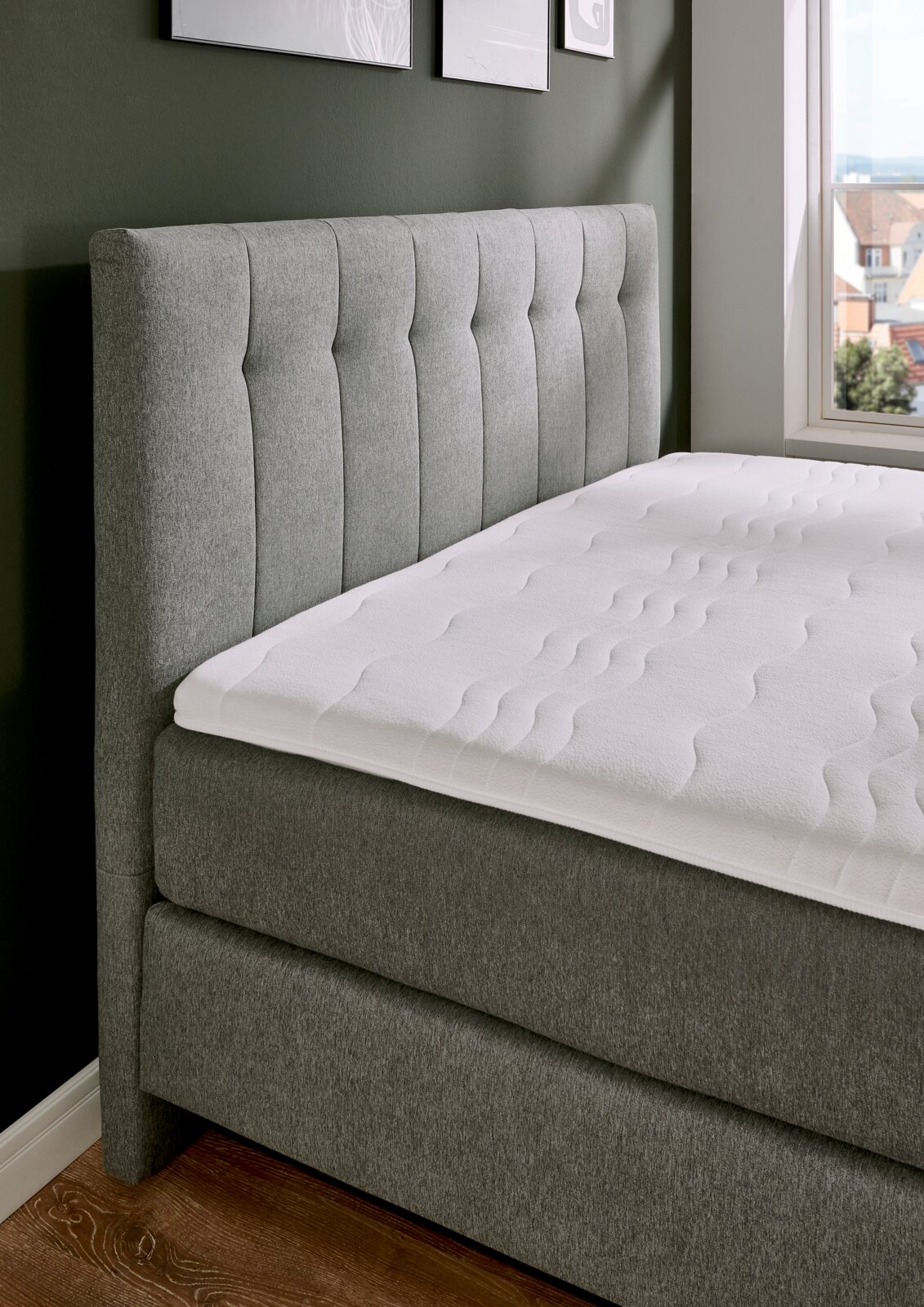 Boxspringbett BX 180/200 in grauem Stoffbezug, seitliche Perspektive mit Blick auf das gepolsterte Kopfteil und die Matratze.