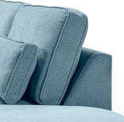 Nahaufnahme eines hellblauen, gepolsterten Sofas mit weichem Stoffbezug, sichtbaren Nähten und Kissen, seitliche Perspektive