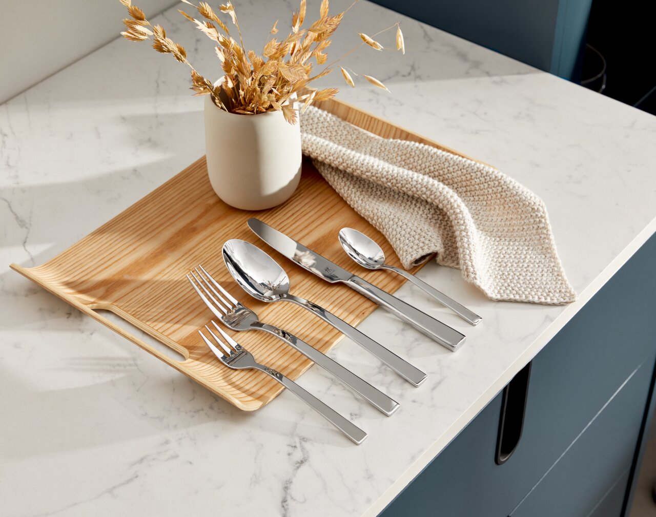 Elegantes Besteckset King 30-tlg. auf einem Holztablett, von oben fotografiert, mit dekorativer Vase und Stoffserviette.