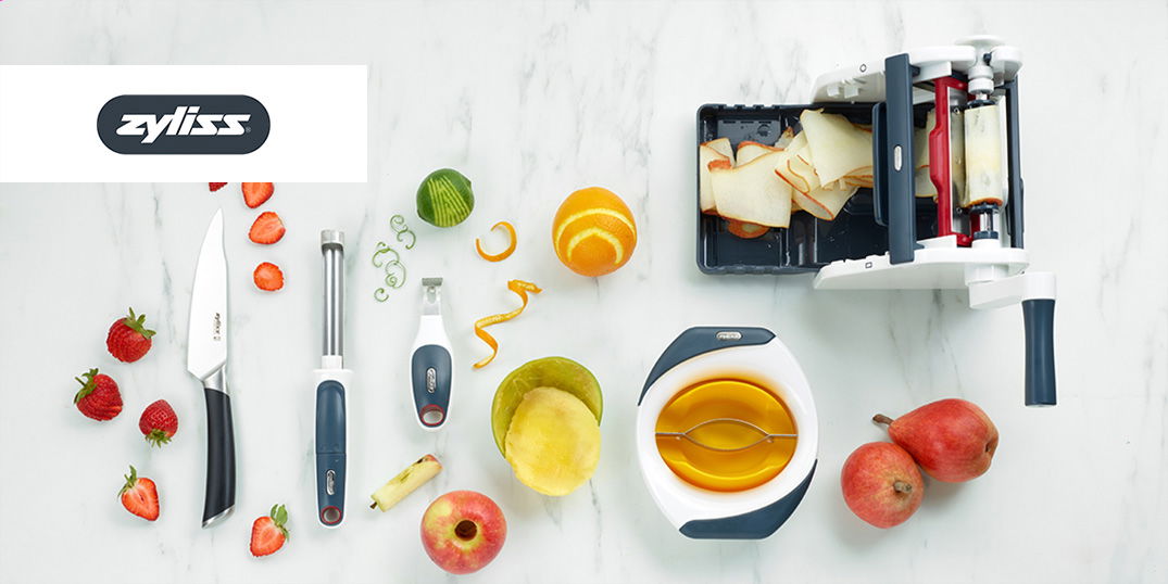 Verschiedene Küchenwerkzeuge und geschnittenes Obst auf einer weißen Marmorplatte.